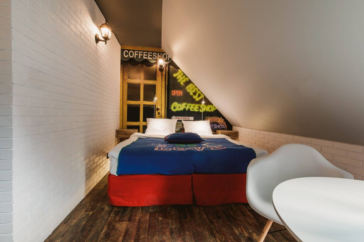 Una habitación acogedora con una cama, una silla blanca y un letrero de cafetería en la pared.