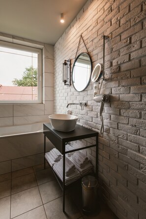 A bathroom with a white brick wall, a round mirror, a sink, and a window.