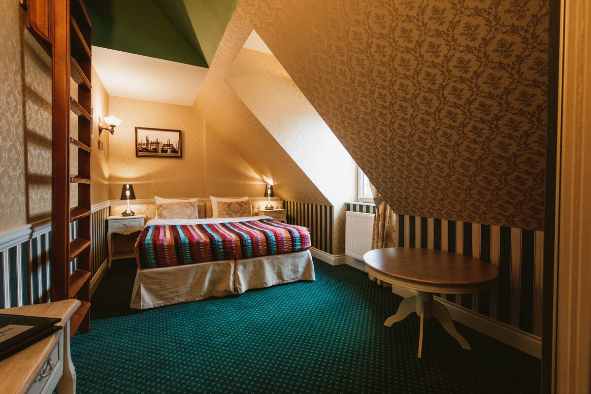 Un dormitorio con cama, mesita de noche, lámpara y una pequeña mesa.