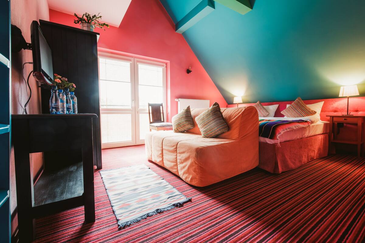 Un dormitorio con una decoración en tonos rojo y azul, un sofá cama, una mesita pequeña y un televisor sobre un soporte.