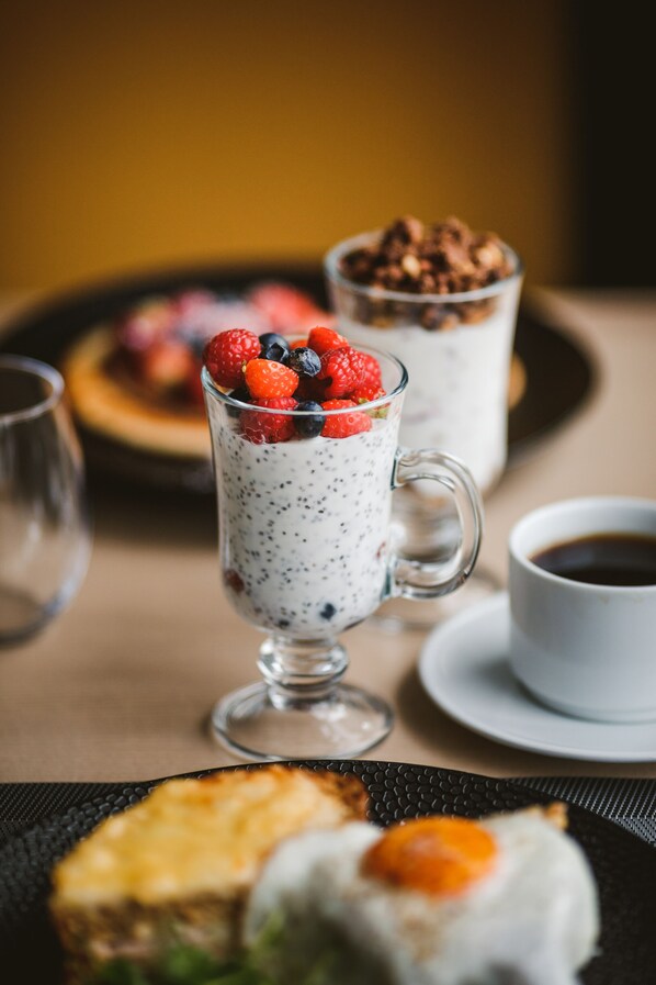 A dessert setting with a glass of yogurt topped with berries, a cup of coffee, and a plate with a piece of cake and an egg.