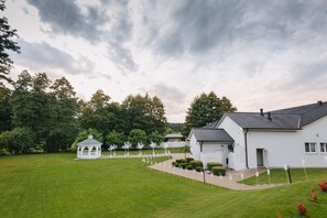 A white building with a tiled roof, surrounded by a well-maintained lawn and trees.
