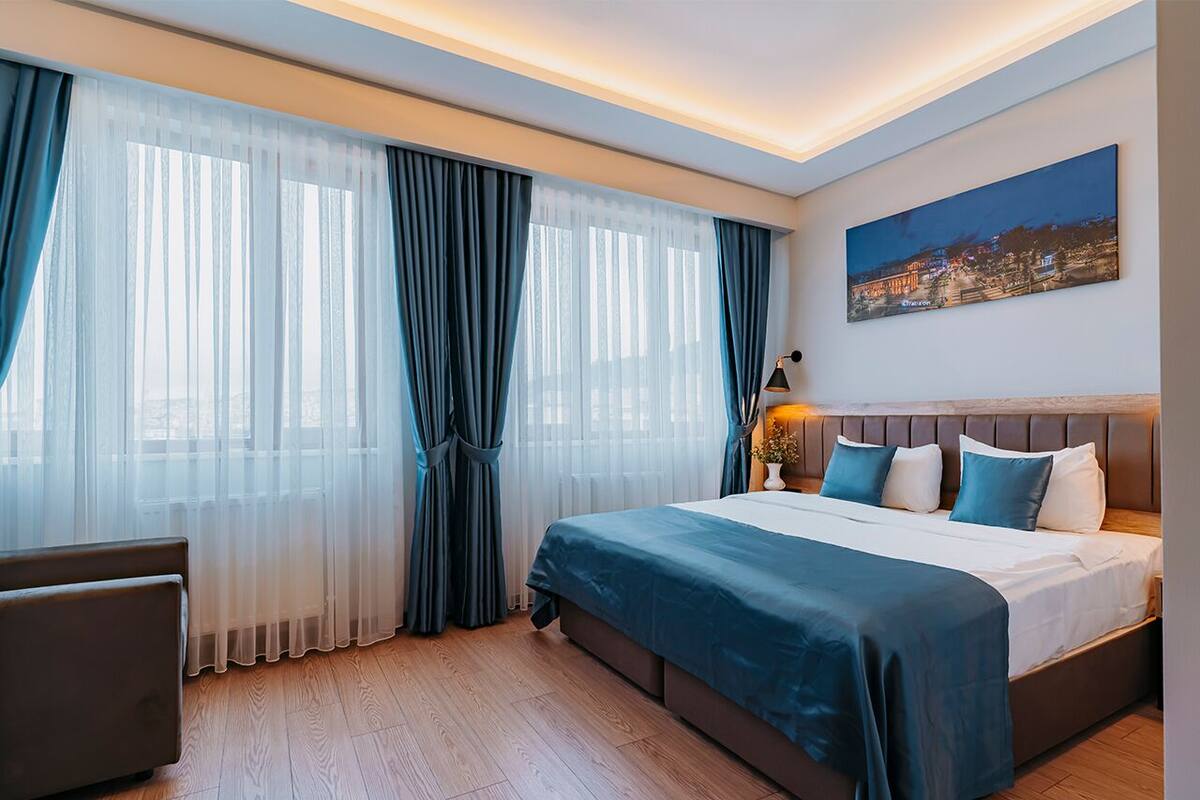 Ett modernt hotellrum med en stor säng, ett skrivbord och en tavla med ett stadsmotiv på väggen.