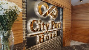 Vastaanottoalue, jossa on City Port -hotellin kyltti, puuseinä ja maljakko täynnä kukkia.