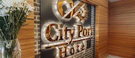 A reception area with a sign for City Port Hotel, a wooden wall, and a vase of flowers.