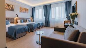 Moderni hotellihuone, jossa on kaksi sänkyä, sohva, pyöreä pöytä ja televisio.