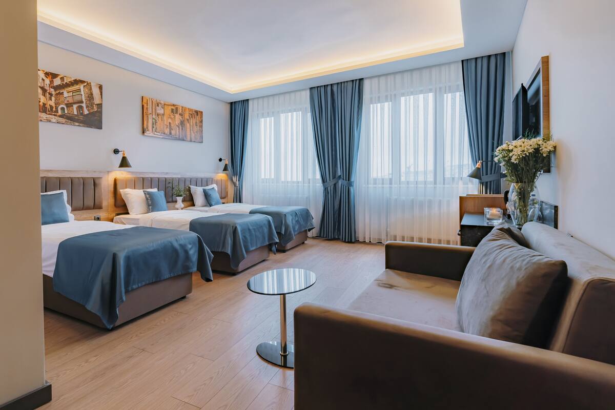 Ett modernt hotellrum med två sängar, en soffa, ett runt bord och en TV.