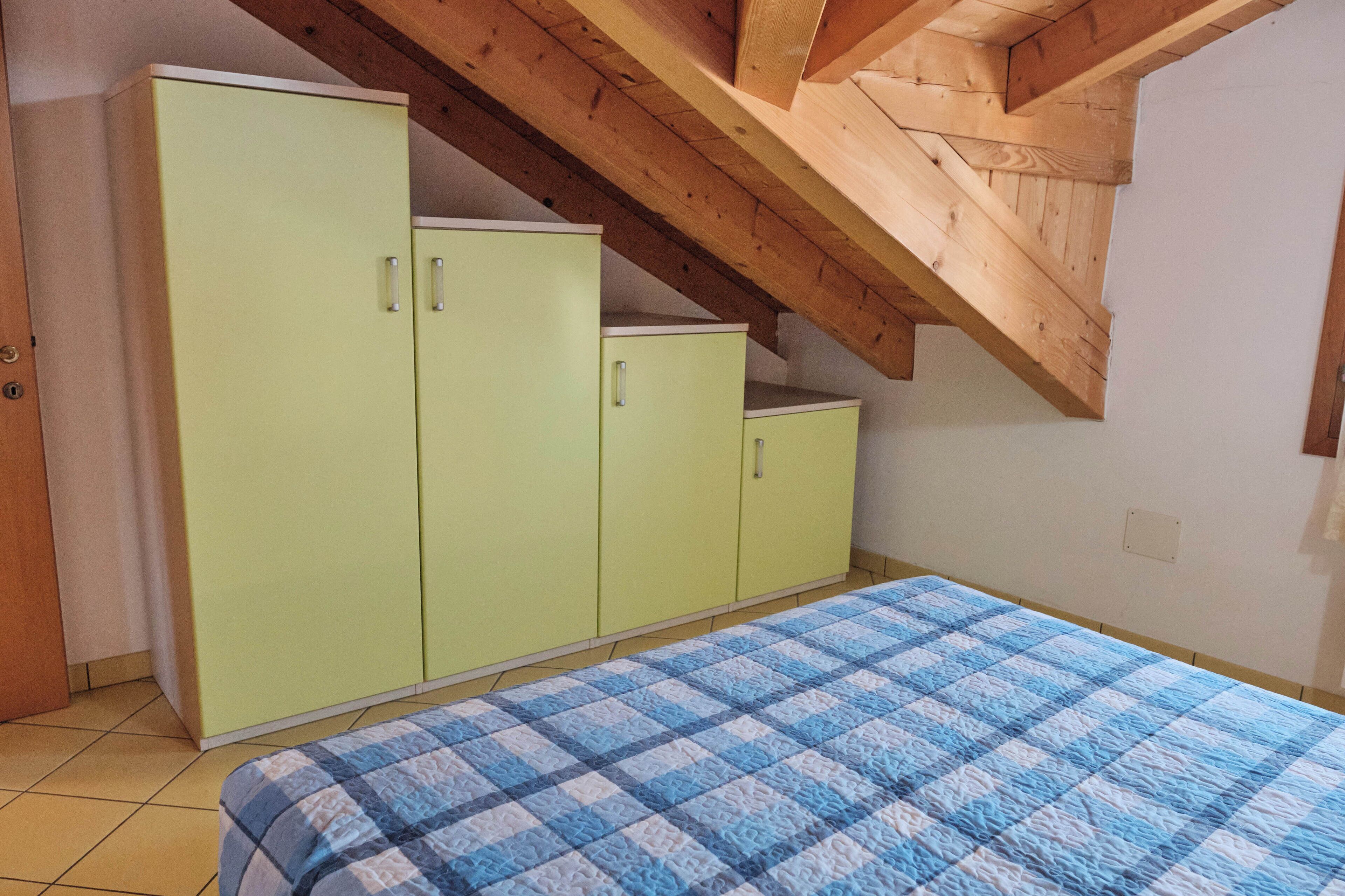 A bedroom with a bed, a green wardrobe, and a sloped ceiling.