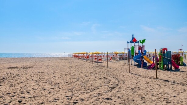 Una playa arenosa con un área de juegos que incluye toboganes coloridos y estructuras recreativas.