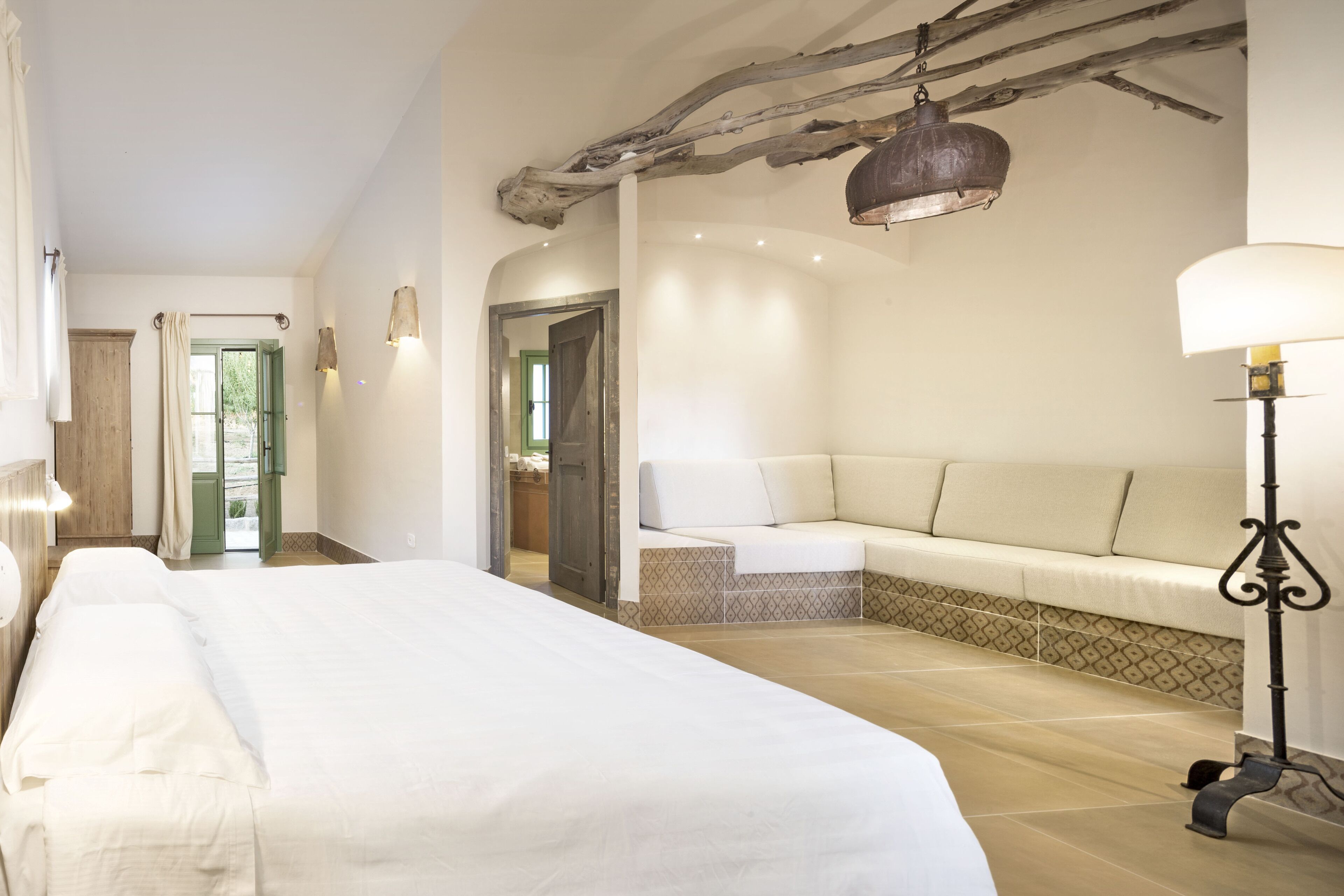 Un dormitorio amplio con una cama grande, una zona de estar con cojines, una lámpara colgante y vistas al exterior.