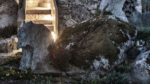 A stone building with a staircase leading to a lit entrance, surrounded by rocks and vegetation. - Gallicantu Stazzo Retreat (Luogosanto)