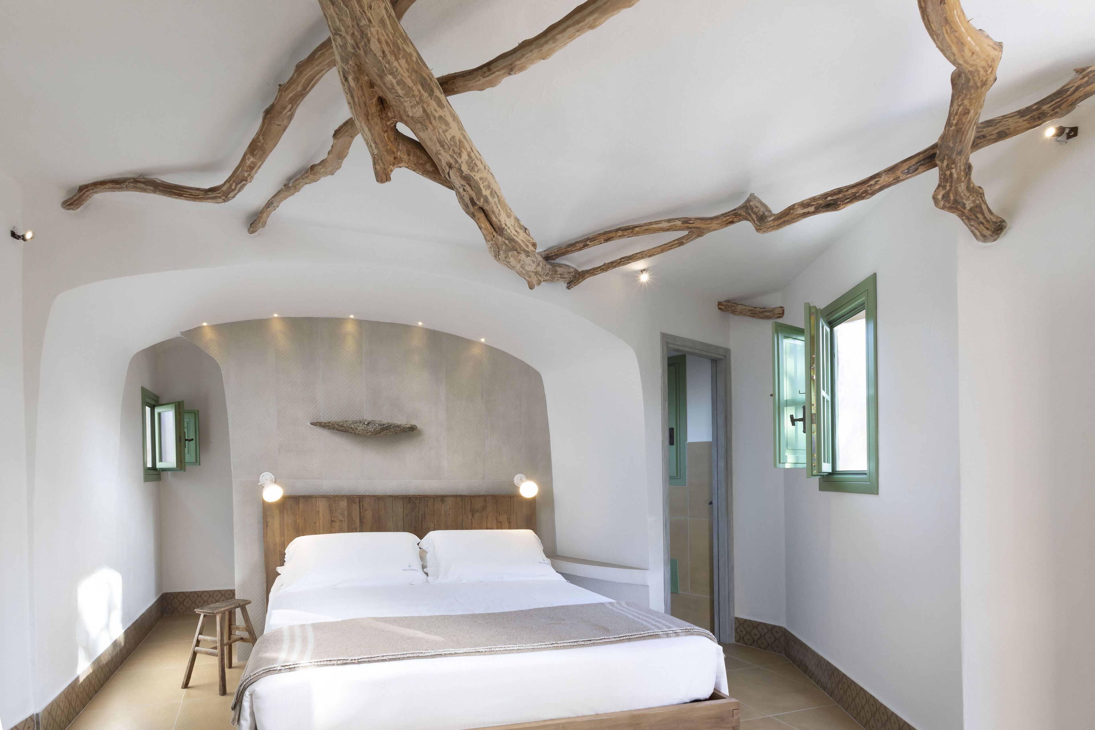 Un dormitori modern amb un llit gran, un amb motlle de fusta i branques d'arbre al descobert com a decoració al sostre.