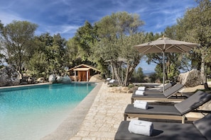 Una piscina al aire libre, sombrillas, sillones reclinables de piscina
