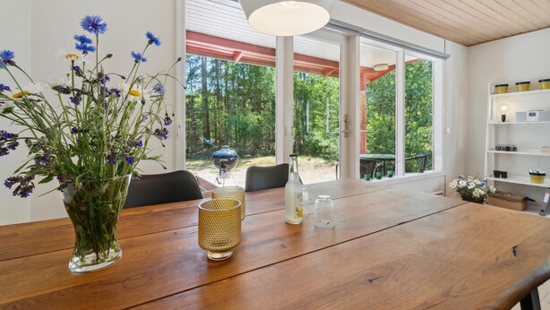 A wooden dining table with a vase of flowers, a glass, and a bottle. - Nice home in Aakirkeby with WiFi (Aakirkeby)