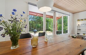 A wooden dining table with a vase of flowers, a glass, and a bottle. - Nice home in Aakirkeby with WiFi (Aakirkeby)