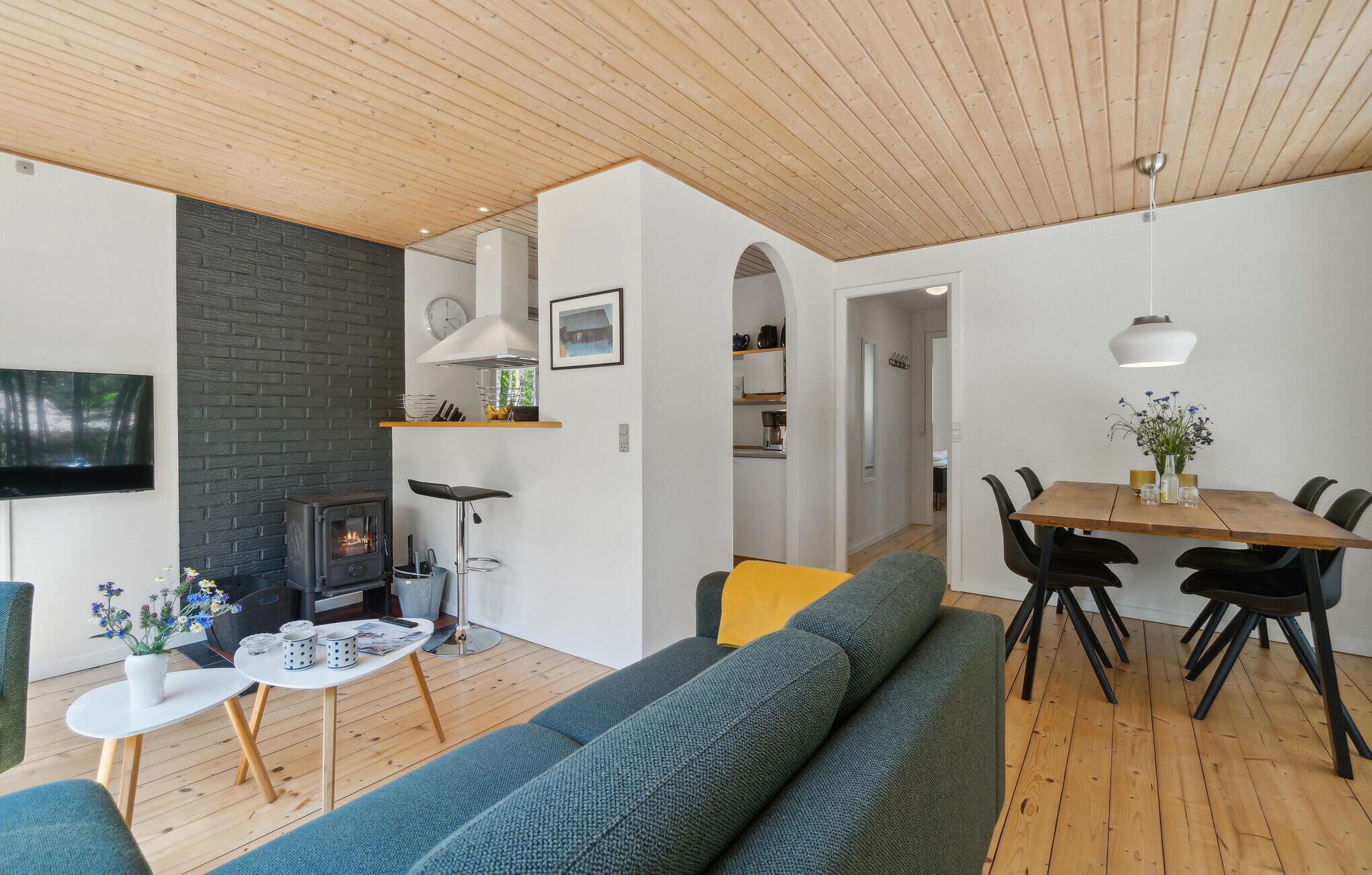 A modern living room with a fireplace, a dining area, and a kitchen visible through an archway.