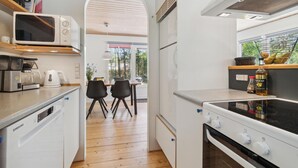A modern kitchen with a microwave, coffee maker, and stove. There is a dining area with chairs and a table, and a view of the outdoors through a large window. - Nice home in Aakirkeby with WiFi (Aakirkeby)