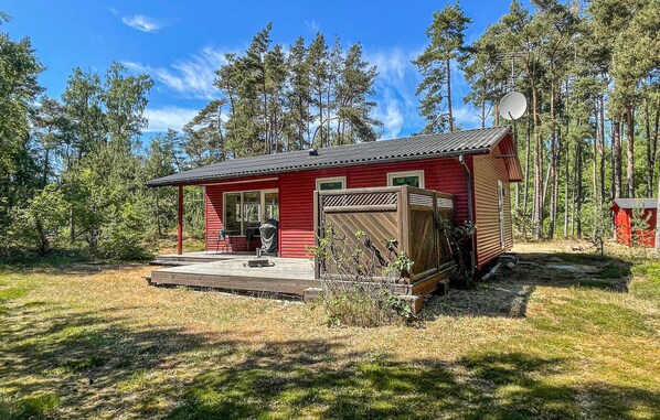 A small, red cabin with a porch, surrounded by a forest. - Nice home in Aakirkeby with WiFi (Aakirkeby)