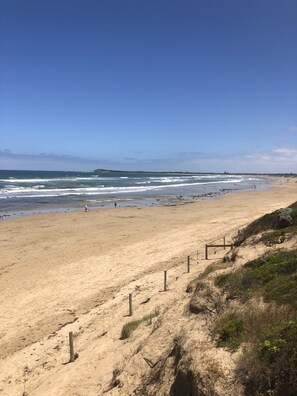 Enjoy a serene beach experience with gentle waves and a natural, grassy dune backdrop.