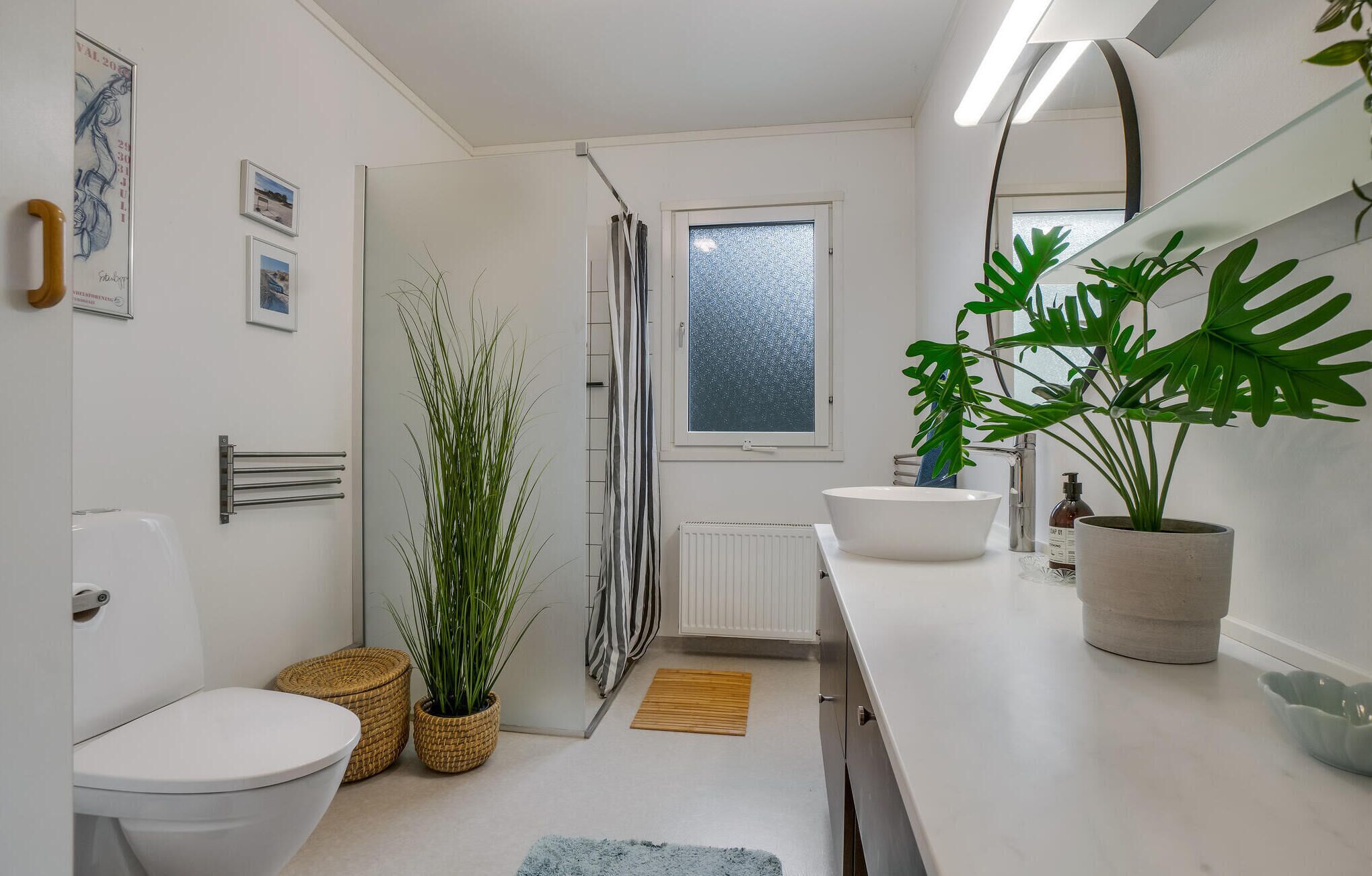 Un baño moderno con inodoro, bidé, ducha y zona de lavamanos. Hay plantas y un espejo en el mostrador.
