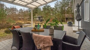 An outdoor patio with a table and chairs, a covered area, and a view of the surrounding forest. - Awesome home in Nexø with WiFi (Nexø)