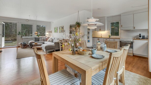 A spacious living area with a wooden dining table, chairs, and a sofa. There is a kitchen area with cabinets and a window. - Awesome home in Nexø with WiFi (Nexø)