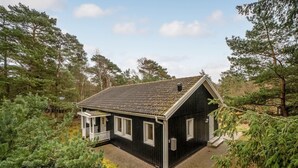 A small, dark wooden cabin with a sloped roof, surrounded by dense pine trees. - Awesome home in Nexø with WiFi (Nexø)