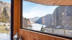 A room with a large window overlooking a river and mountains.