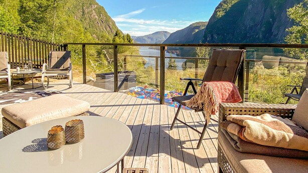 A wooden deck with outdoor furniture, a glass balustrade, and a view of a valley and river.