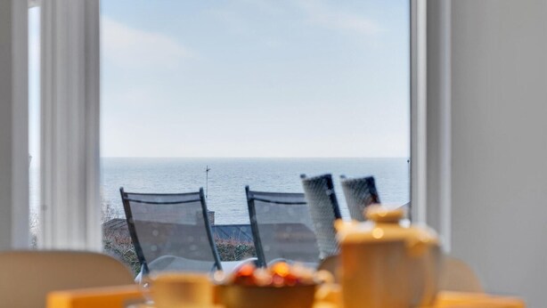 Une vue depuis une fenêtre donnant sur une plage, avec deux chaises et une table au premier plan.