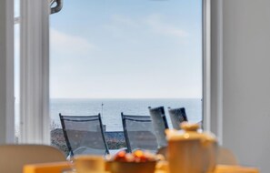 Vista da janela com uma praia à mostra, com duas cadeiras e uma mesa em primeiro plano.