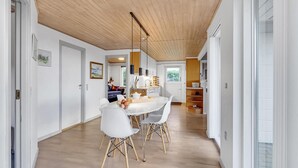 Une cuisine moderne avec des meubles blancs, un plafond en bois et un coin repas comprenant des chaises blanches et une table blanche.