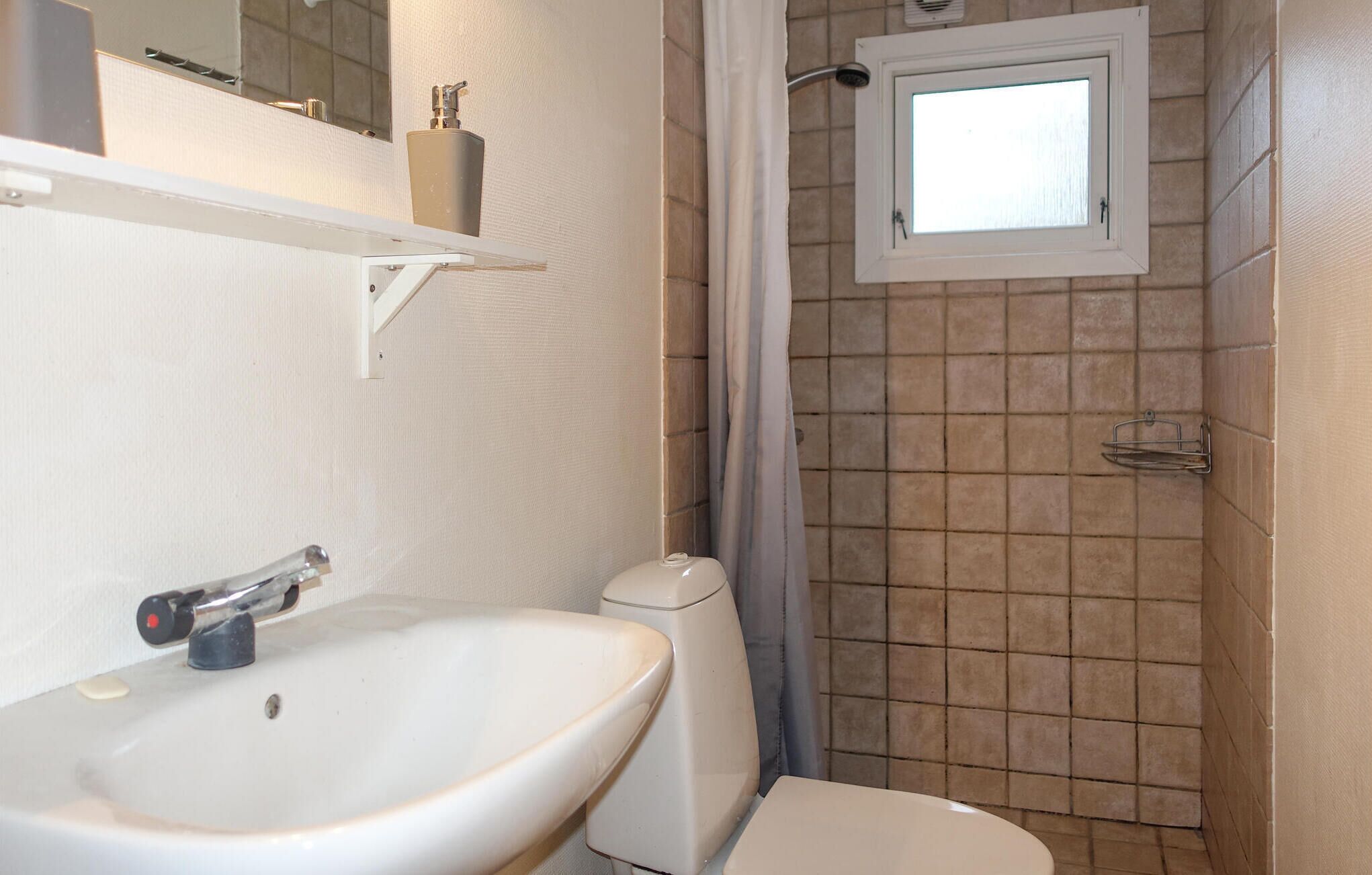 A bathroom with a white sink, a toilet, a shower with a glass door, and a small window above the shower.