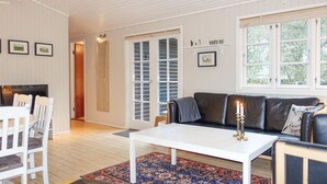 A living room with a white coffee table, a black leather sofa, a patterned rug, and a dining area with white chairs. - Stunning home in Aakirkeby with WiFi (Aakirkeby)