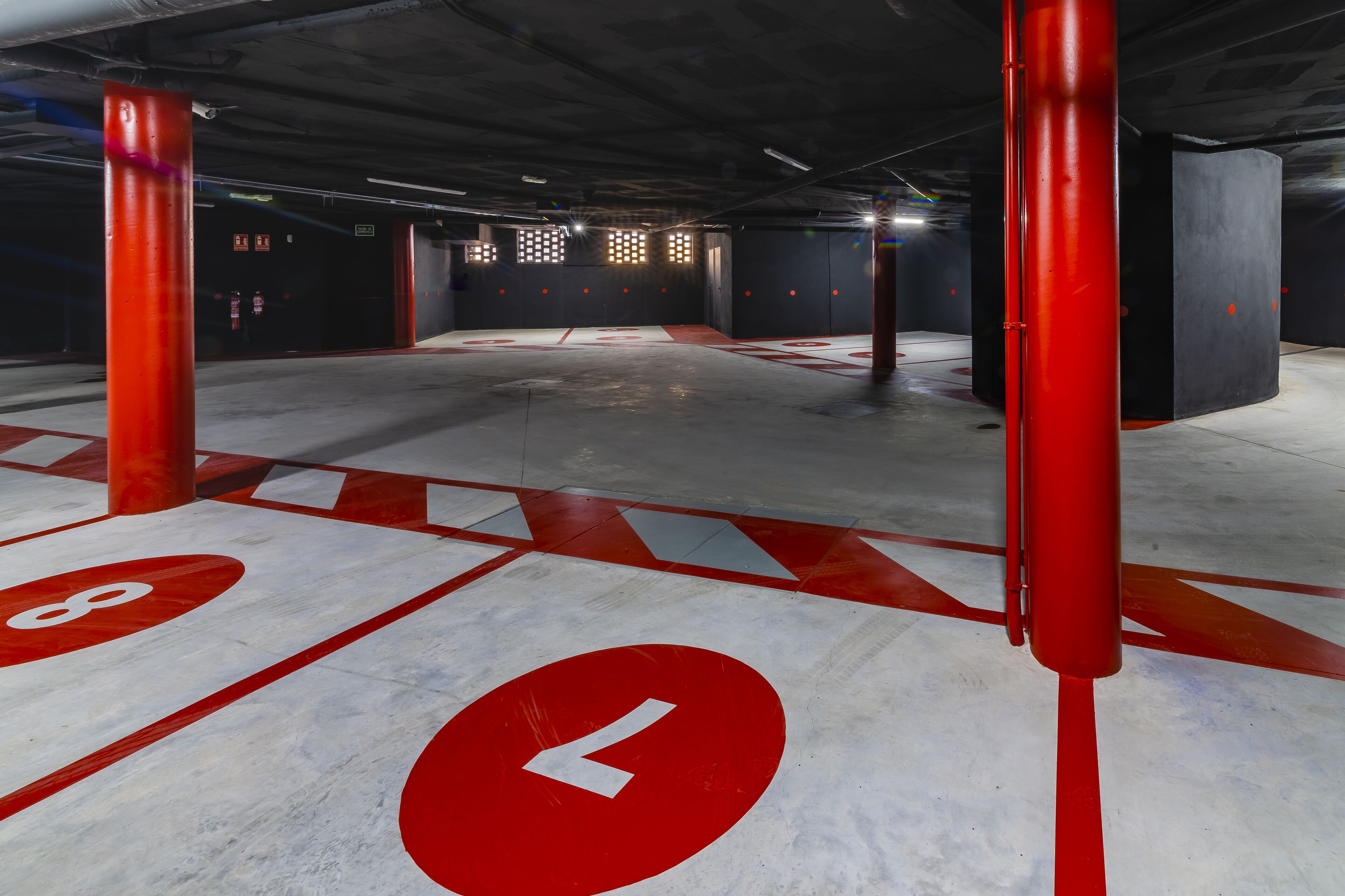 Eine Innenparkgarage mit roten Säulen, Pfeilen zur Orientierung und nummerierten Stellplätzen.