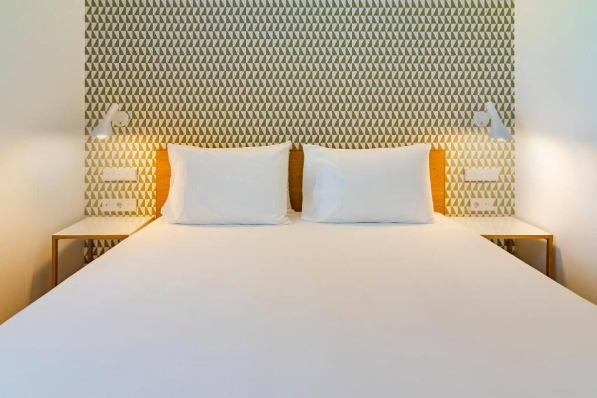 Een bed met een hoofdbord met een geometrisch patroon, twee nachtkastjes met lampen en een effen witte spreidekker.