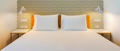 Una cama con cabecera de diseño geométrico, dos mesitas de noche con lámparas y un edredón blanco liso.