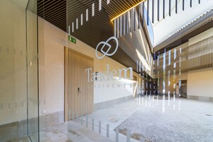 A spacious indoor corridor with a modern design, featuring a glass wall, a wooden door, and a sign for 'Tandem Apartments'.