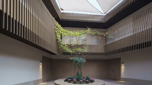 Een moderne atriumruimte met een centrale tuin, verticale lamellenwanden en een dakraam.