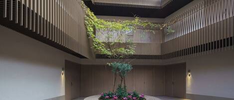 Un atrium moderne doté d’un jardin central, de murs à lattes verticales et d’une verrière.