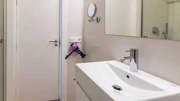 A bathroom with a white sink, a mirror, and a hairdryer mounted on the wall.