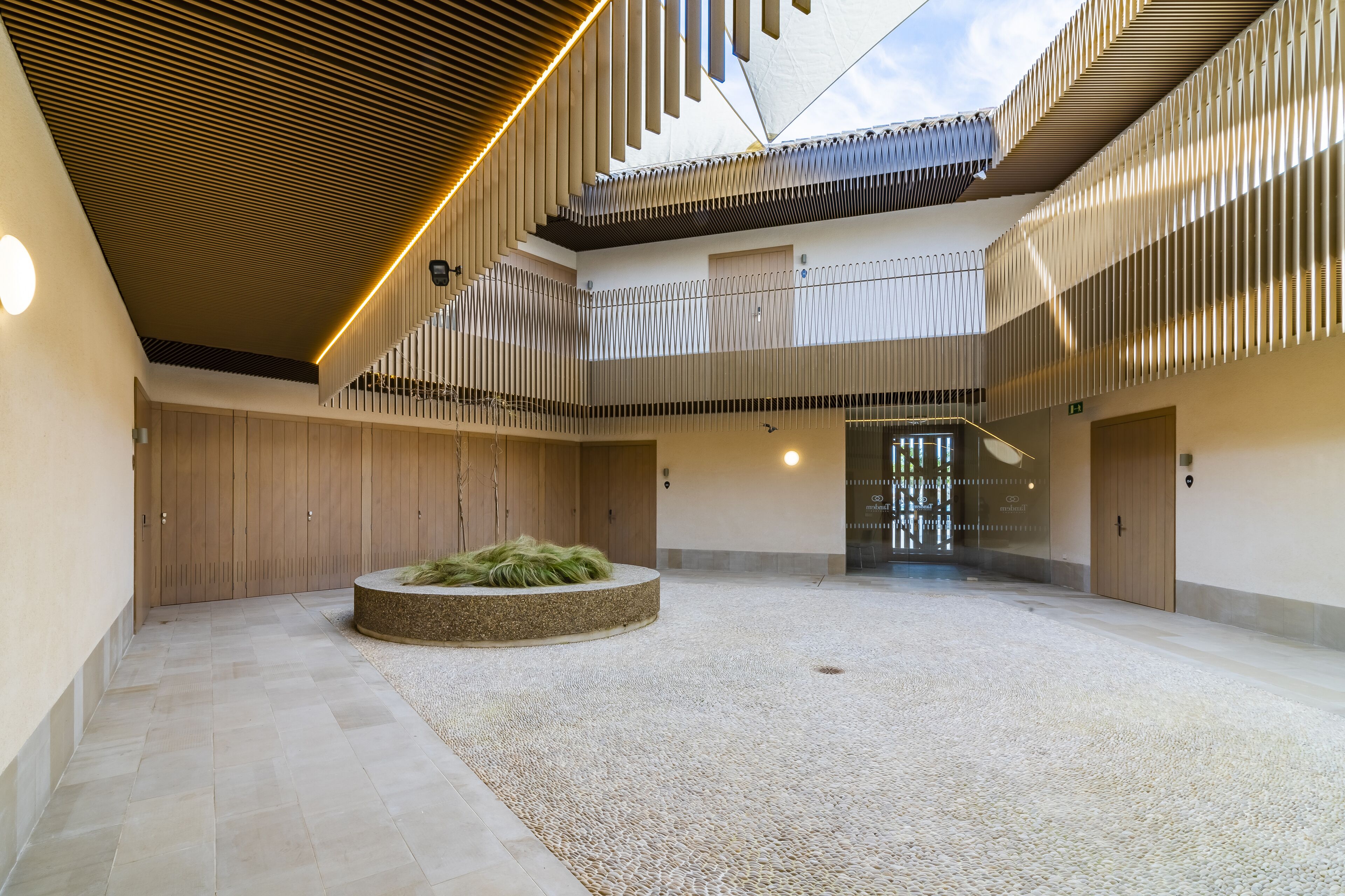 A spacious atrium with a high ceiling, a central circular seating area, and a modern design with wooden slats and recessed lighting.