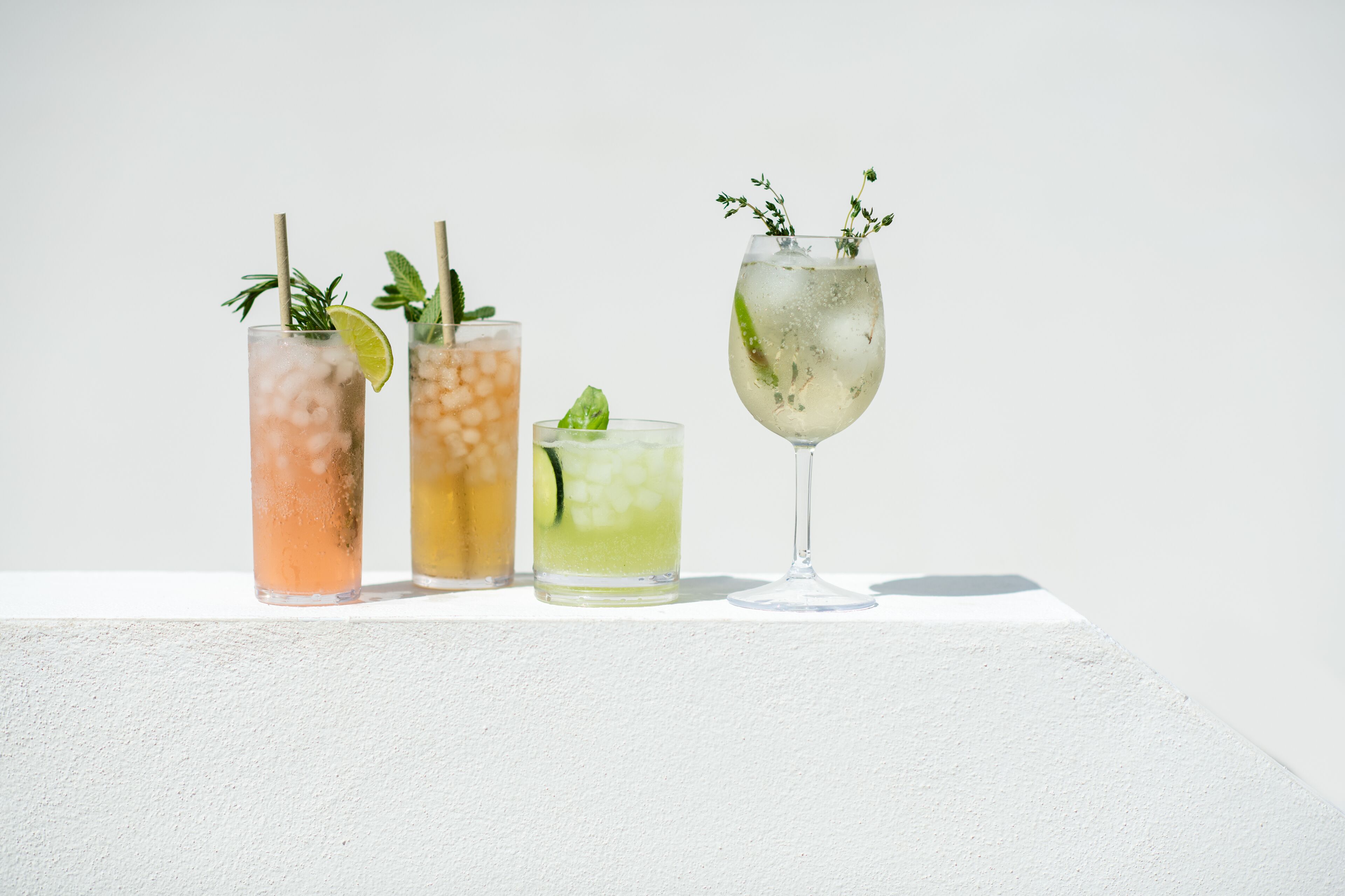 Fyra glas med iskalla drycker, garnerade med mynta och lime, står på en vit yta.