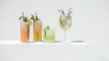 Fyra glas med iskalla drycker, garnerade med mynta och lime, står på en vit yta.