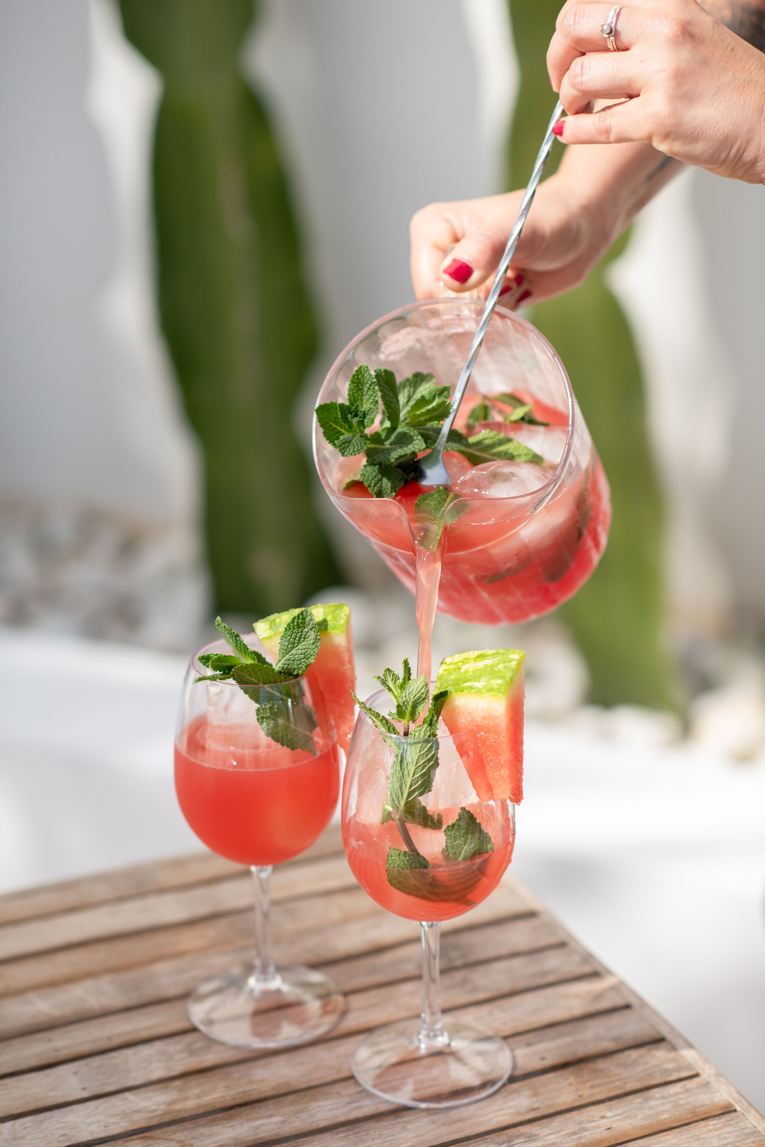 Tres vasos de cóctel rosado con hojas de menta sobre una mesa de madera.
