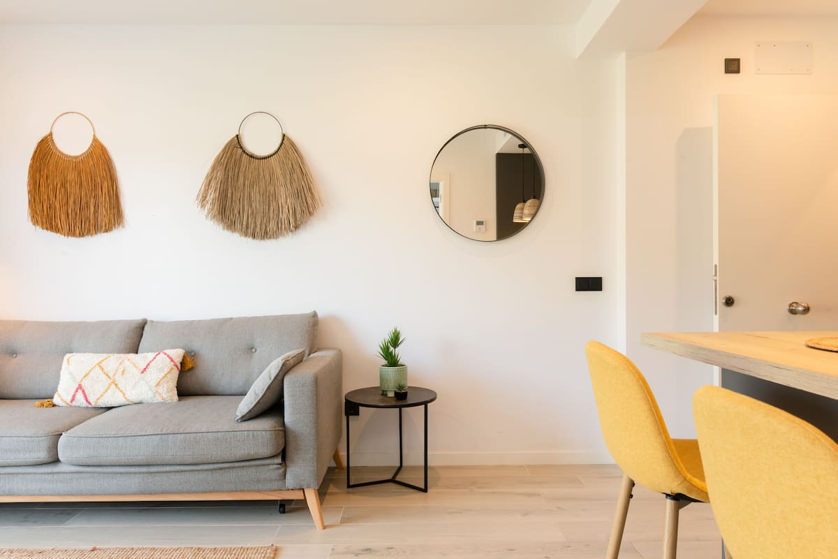 A modern living room with a grey sofa, a small round side table with a plant, and a yellow chair.