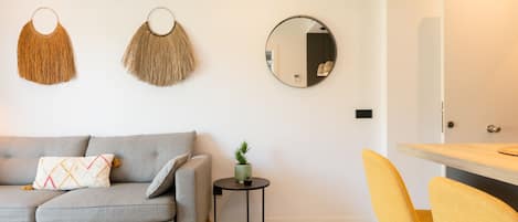 A modern living room with a grey sofa, a small round side table with a plant, and a yellow chair.