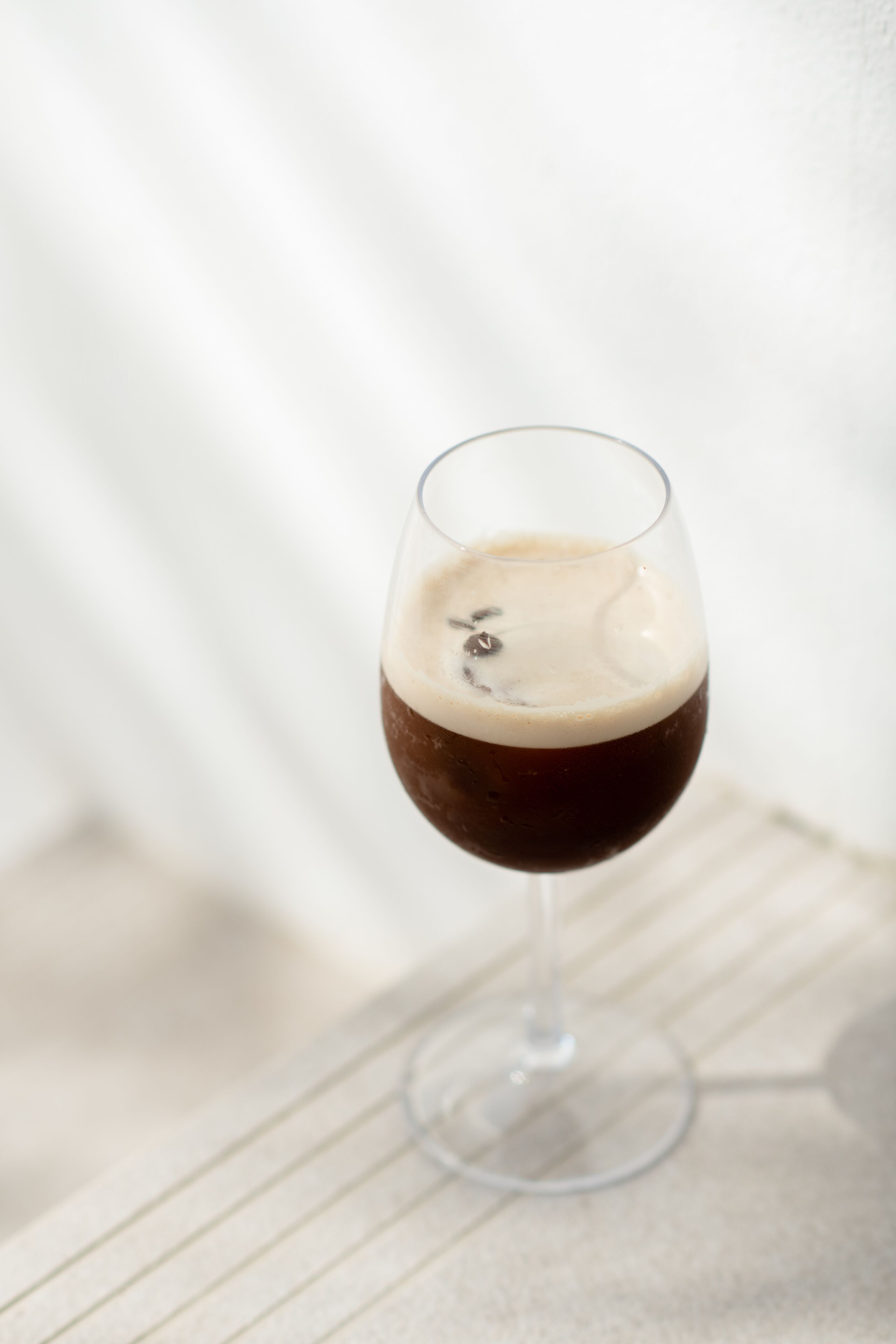 A glass of dark liquid with a frothy top on a table.