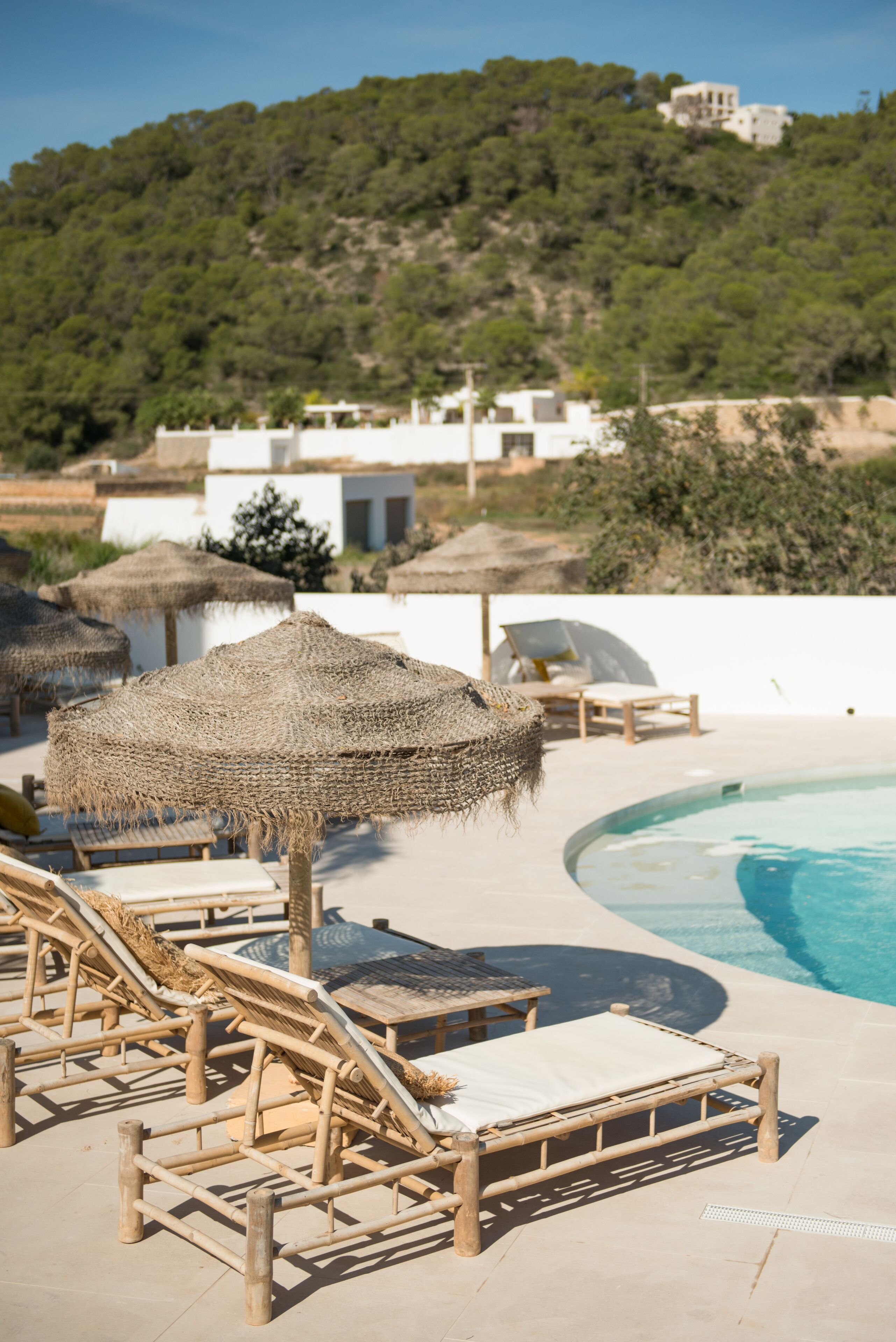 A poolside area with lounge chairs, a thatched umbrella, and a view of a hillside with buildings.