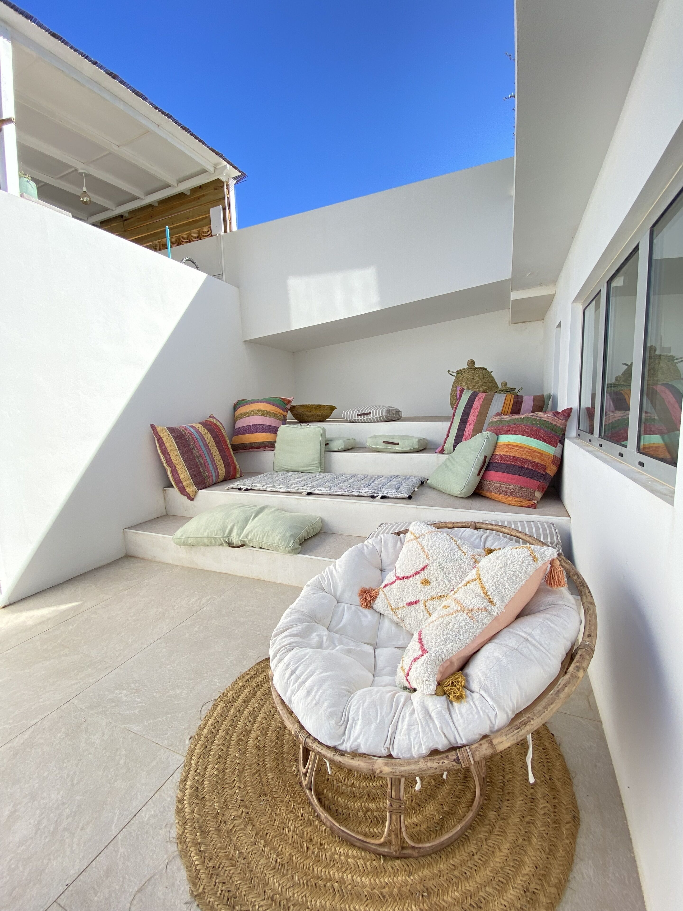 A modern outdoor seating area with a wicker chair and cushions, a woven mat, and a variety of pillows.